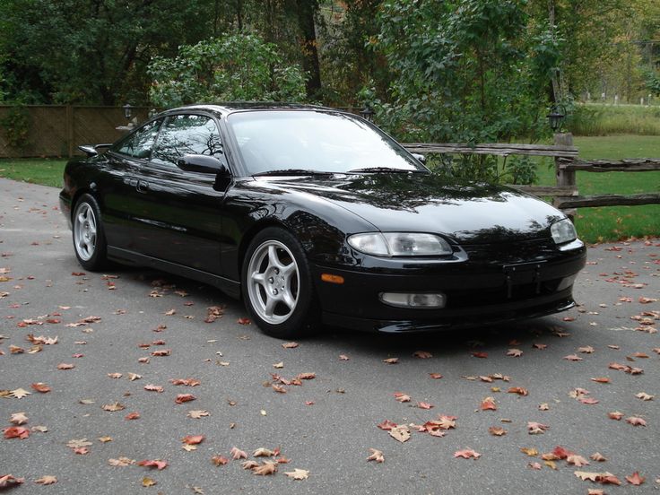 a black sports car parked in front of a wooden fence and some leaves on the ground