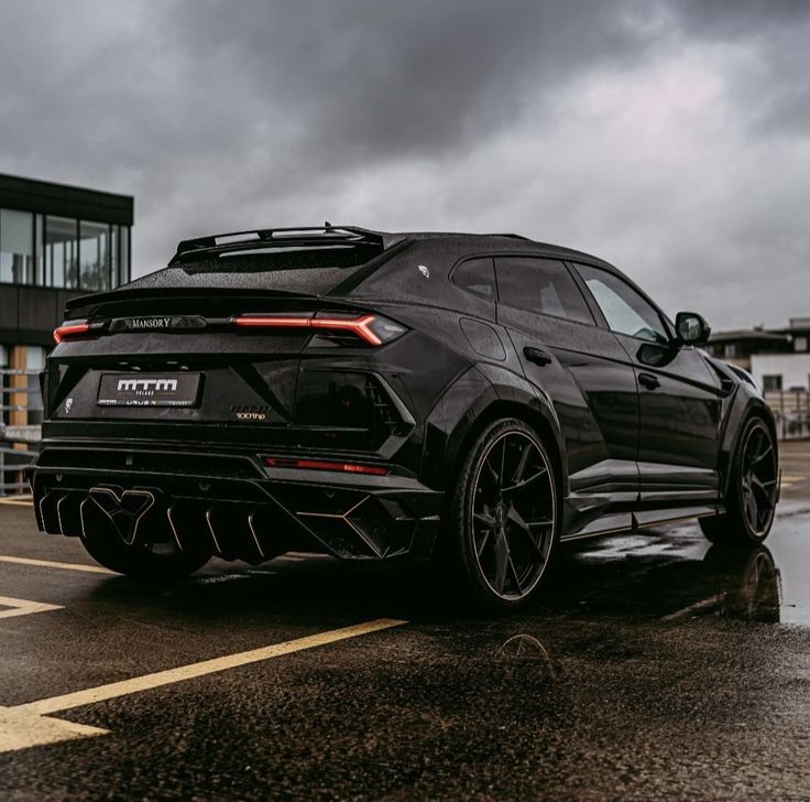 the rear end of a black sports car parked in a parking lot on a rainy day