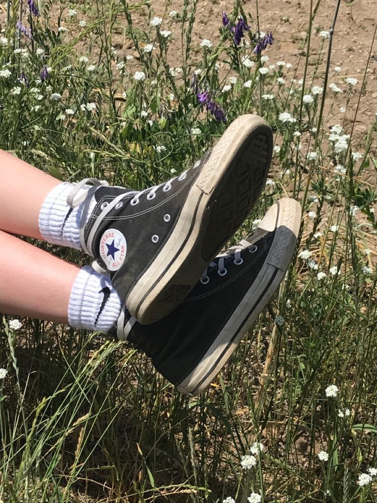 a woman's legs with converse shoes in the grass and wildflowers behind her