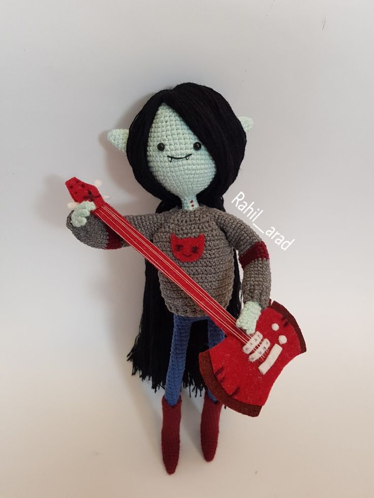 a crocheted doll holding a red guitar and wearing a black wig with horns