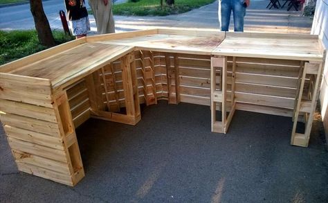 a wooden bench made out of pallets on the side of a road with people walking by