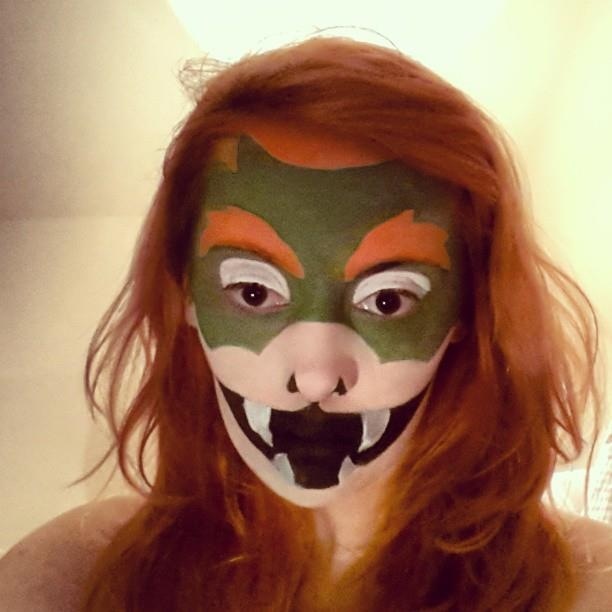 a woman with red hair wearing a green and orange face paint design on her face