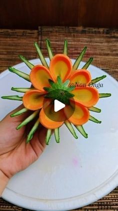 a hand holding a small orange flower on top of a white plate with green stems