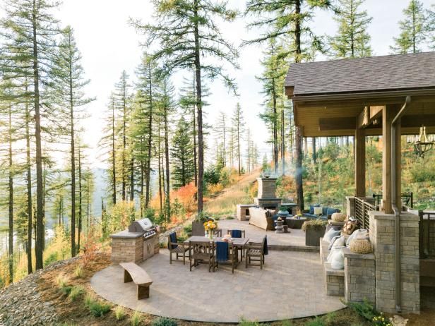 an outdoor patio with table, chairs and grill in the middle surrounded by pine trees