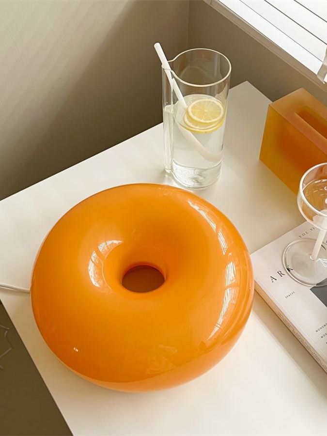 an orange donut sitting on top of a table next to a glass of water