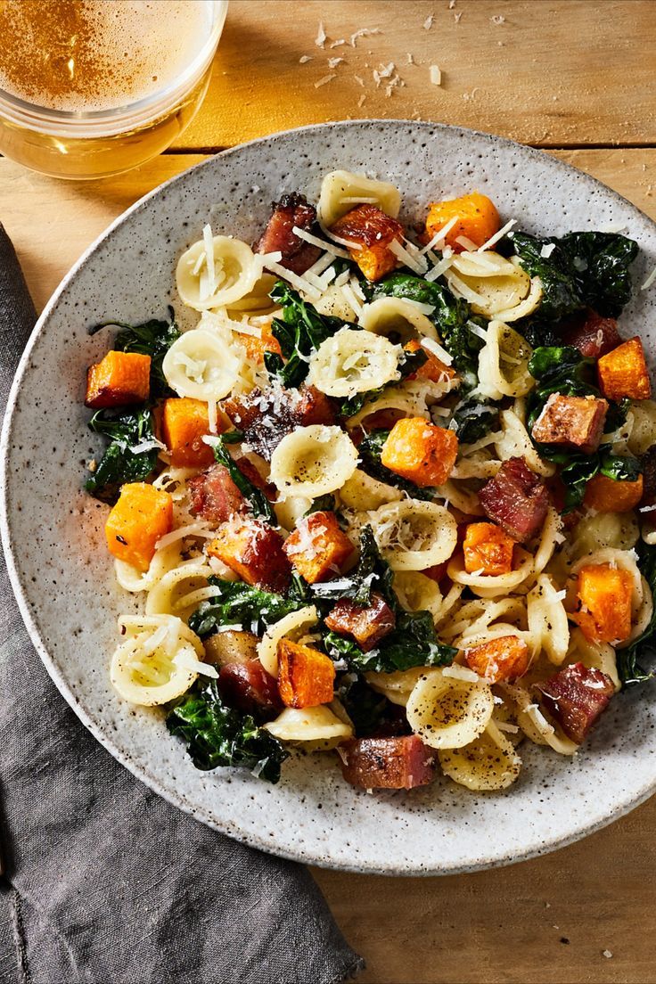 a white bowl filled with pasta and spinach covered in cheese on top of a wooden table