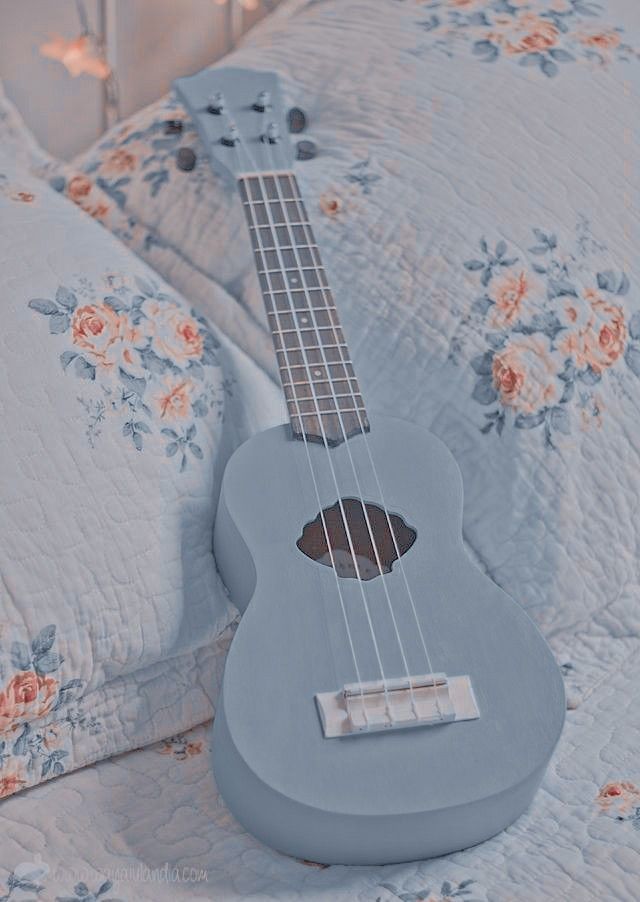 a blue ukulele laying on a bed with pink roses and white sheets in the background