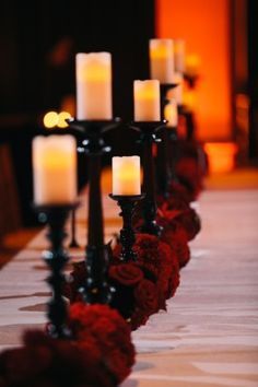 candles are lined up on the table with red flowers