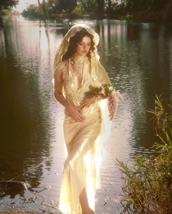 a woman in a wedding dress is standing by the water