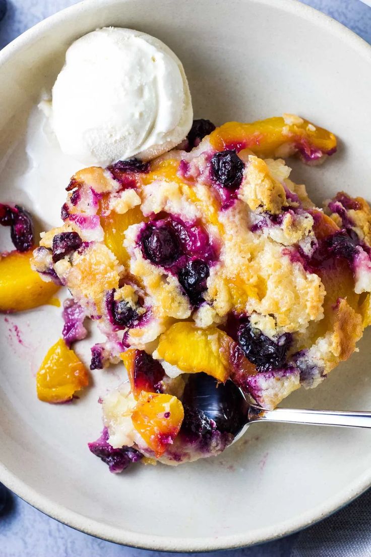 a white plate topped with blueberries and peaches next to a scoop of ice cream