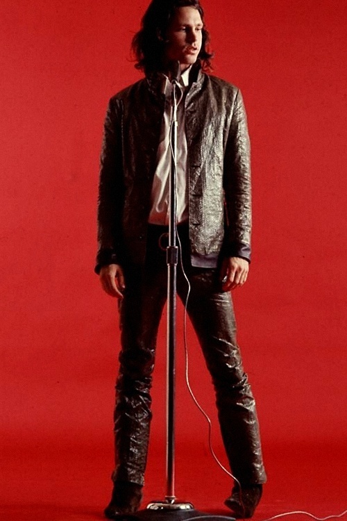 a man standing in front of a microphone on top of a red background with long hair