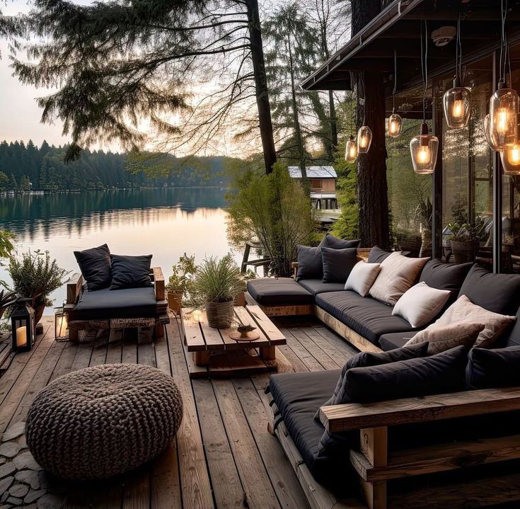 a wooden deck with lots of furniture and lights hanging from it's sides over the water