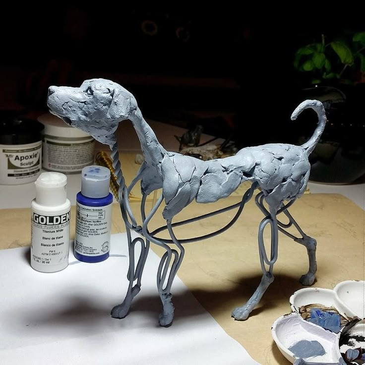 a sculpture of a dog on a table next to some paint bottles and other items