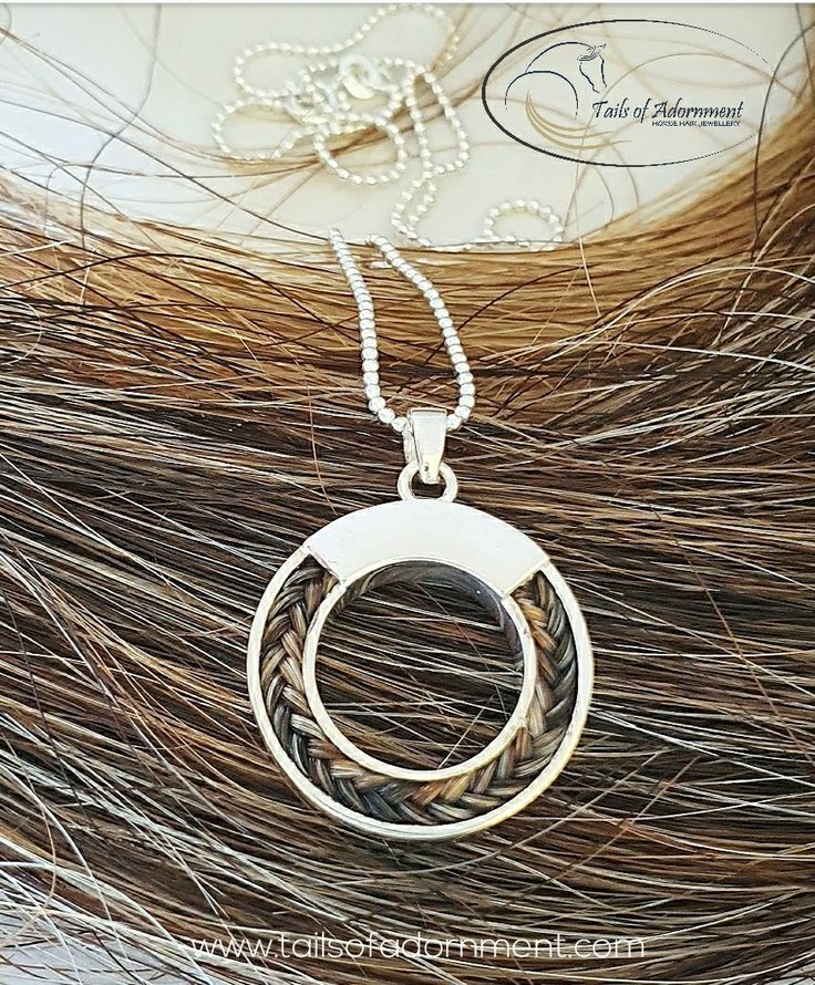 a silver pendant with two rings on top of some long brown and white hair in the background