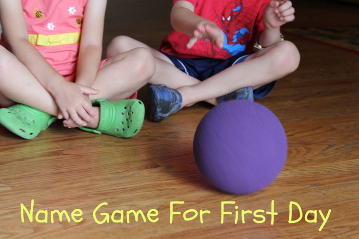 two young children sitting on the floor playing with a purple ball and green rubber boots