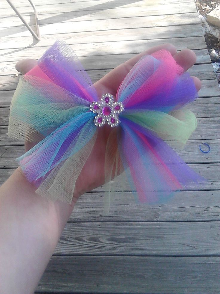 a hand holding a colorful hair bow on top of a wooden deck