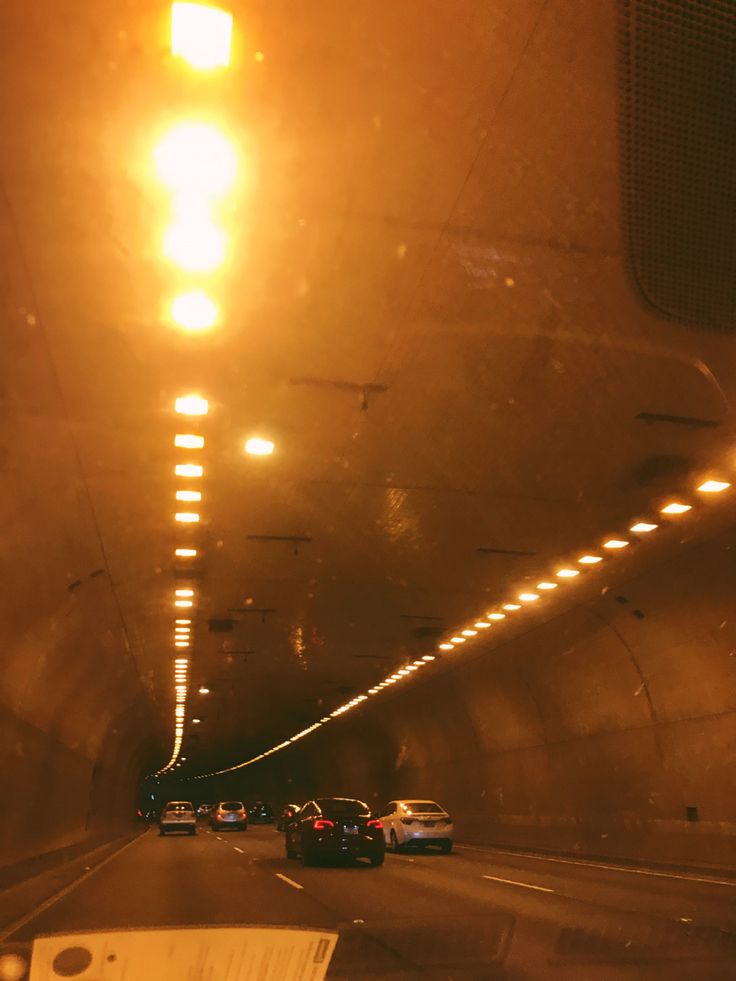 cars driving through a tunnel at night with bright lights on the ceiling and below them