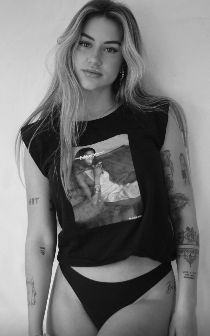 a woman with tattoos on her arms and chest wearing a black shirt that has an image of a man in it