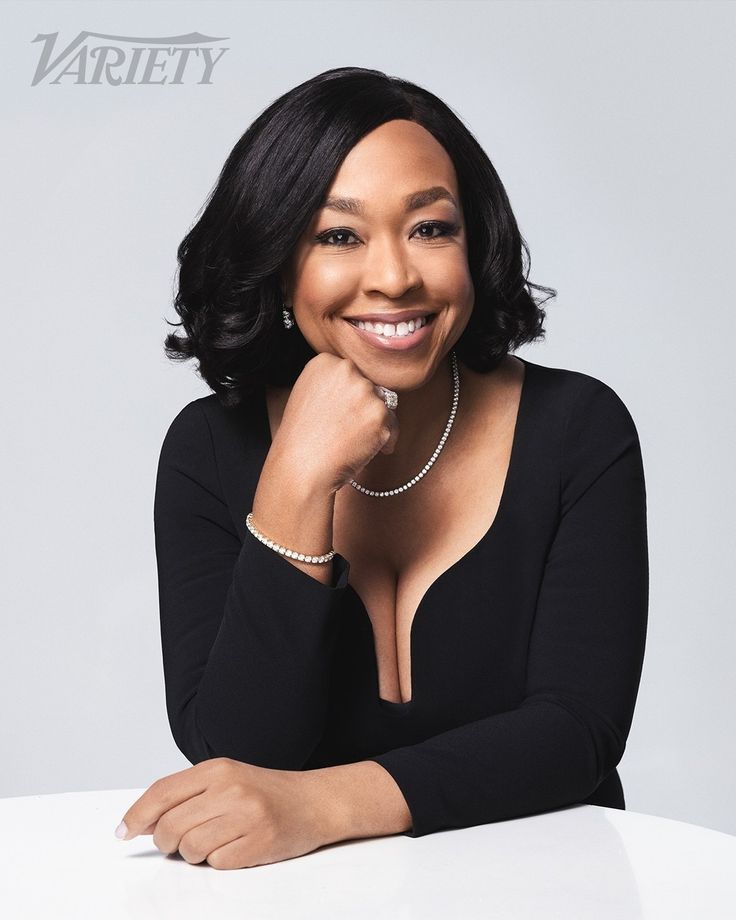 a woman sitting at a table with her hand on her chin and smiling for the camera