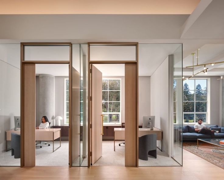 an office with glass walls and wooden floors, two people sitting at desks in the background