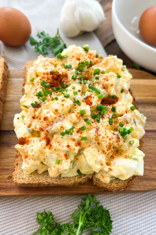 an open face sandwich on a cutting board with eggs and parsley in the background