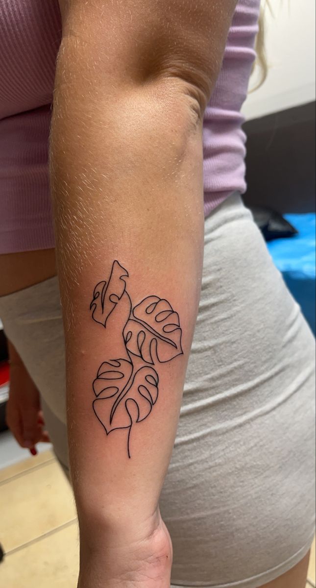 a woman's arm with a tattoo on it that has leaves in black ink