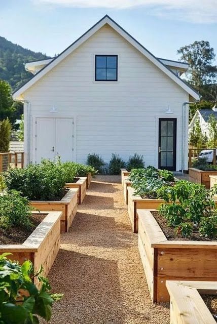 a white house with lots of plants in the front yard and garden beds on both sides