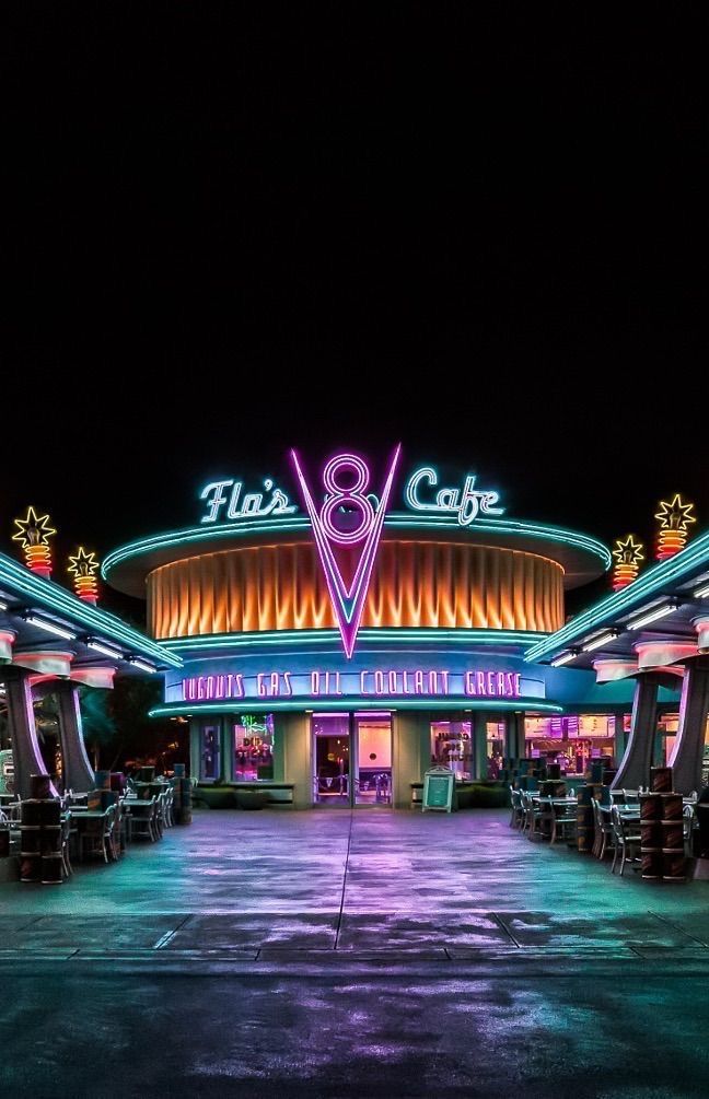 the entrance to an amusement park at night with neon lights on it's sides