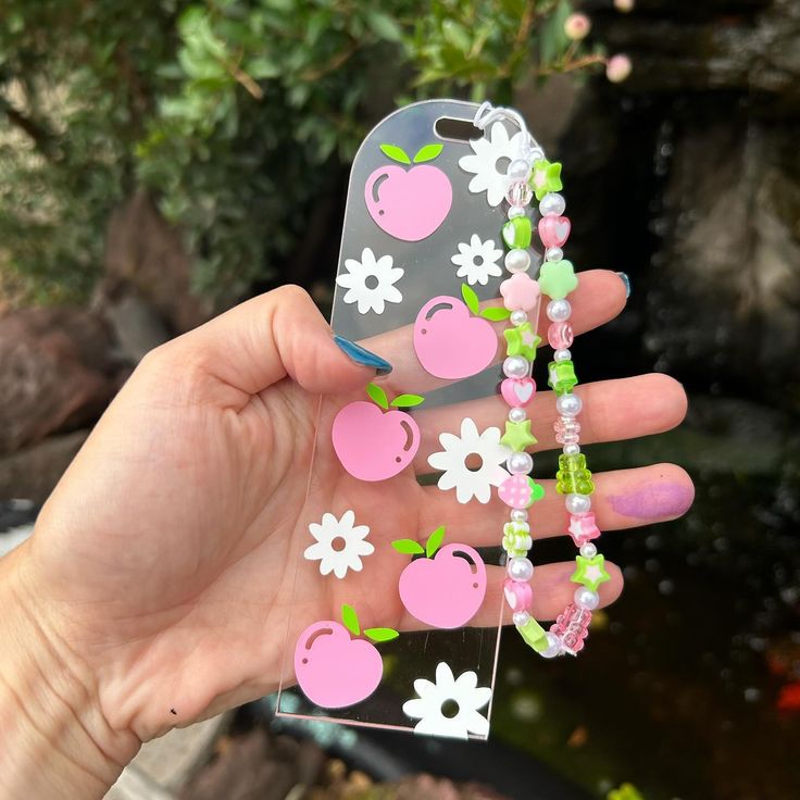 a person holding up a phone case that has fruit and flowers on the front, while standing next to a pond