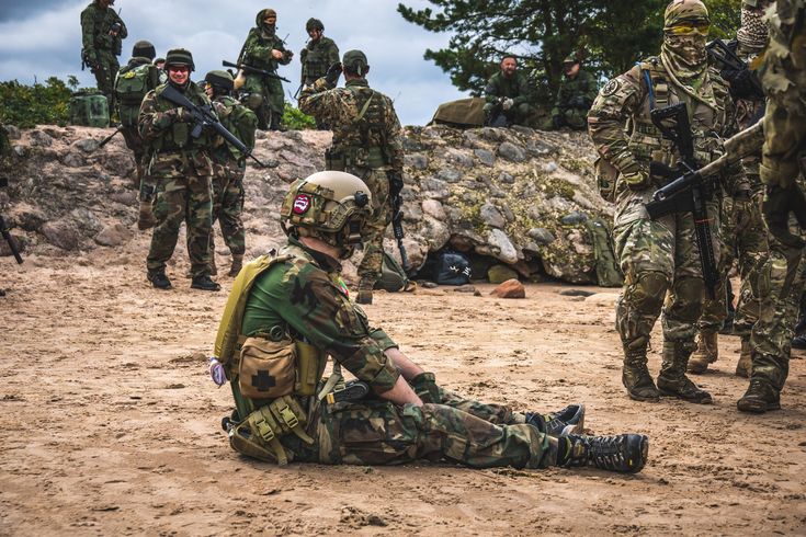 a group of soldiers standing and sitting on top of a dirt field next to each other