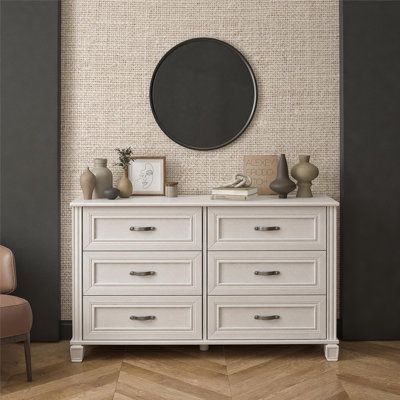 a white dresser sitting next to a chair in a room with a mirror on the wall