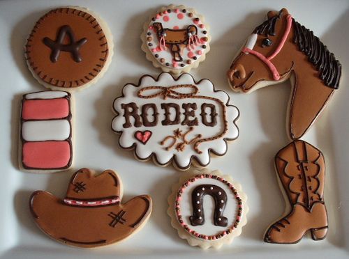 decorated cookies in the shape of horses, cowboy hats, and horseshoes on a plate