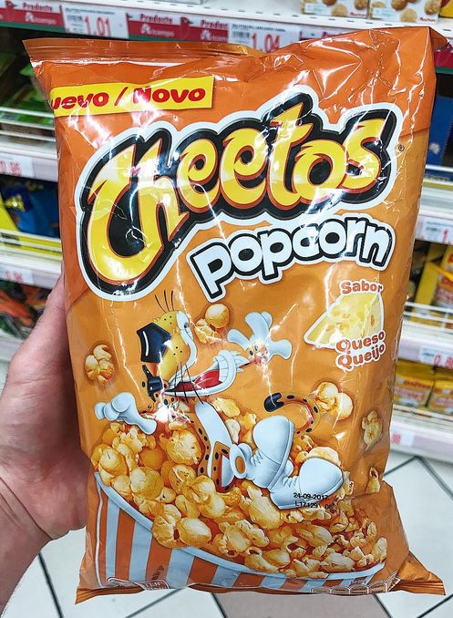 a hand holding a bag of cheetos popcorn in front of a store shelf