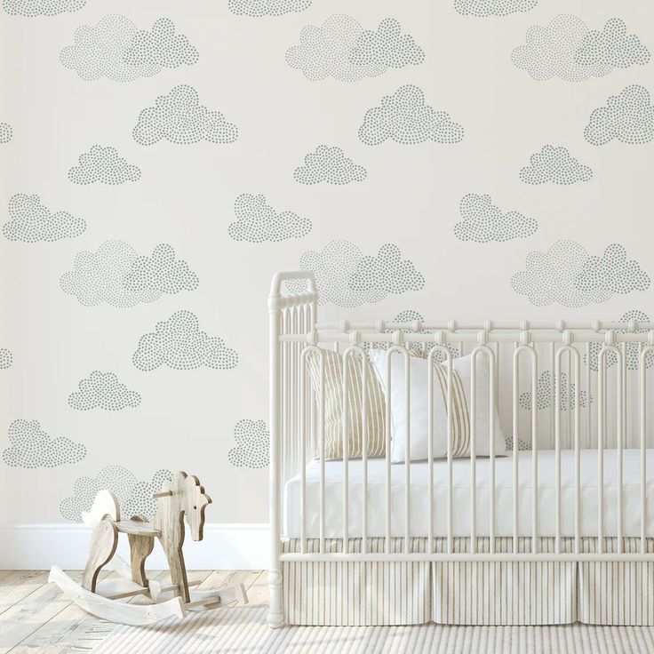 a baby's room with a white crib and wallpaper that has clouds on it