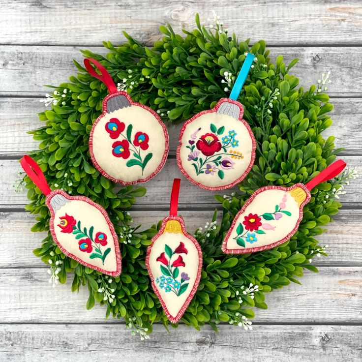 four ornaments are hanging from a wreath on a wooden surface with greenery around them