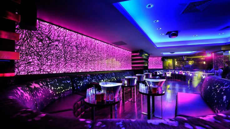 a dimly lit room with purple lighting and round tables in front of the bar area