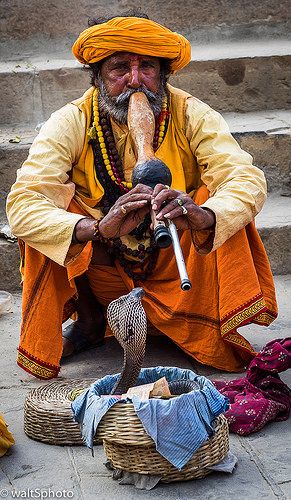 an old man sitting on the ground with a pipe in his mouth and other items around him