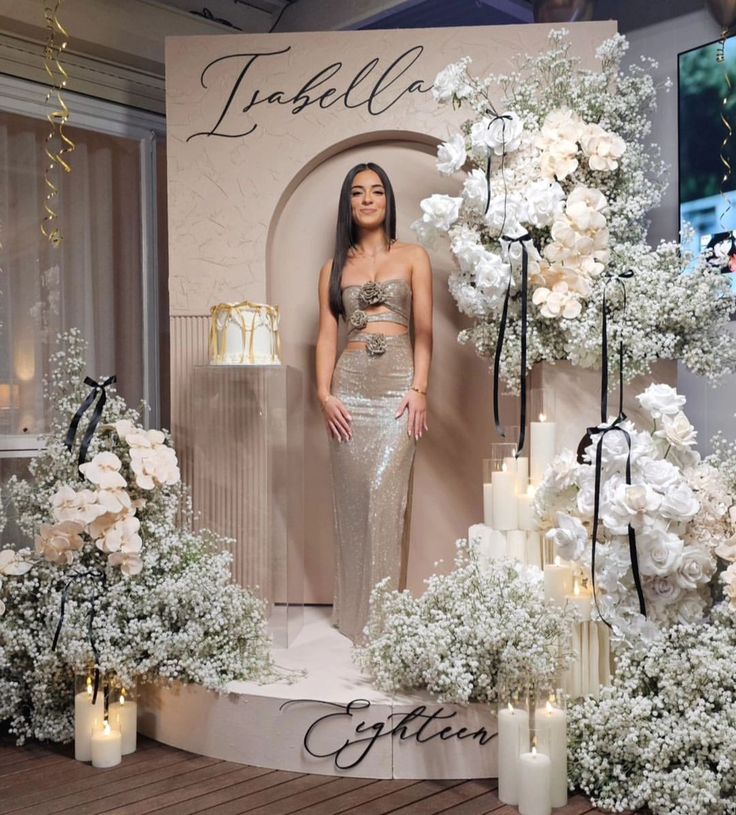 a woman standing in front of a display with white flowers and candles on it's sides