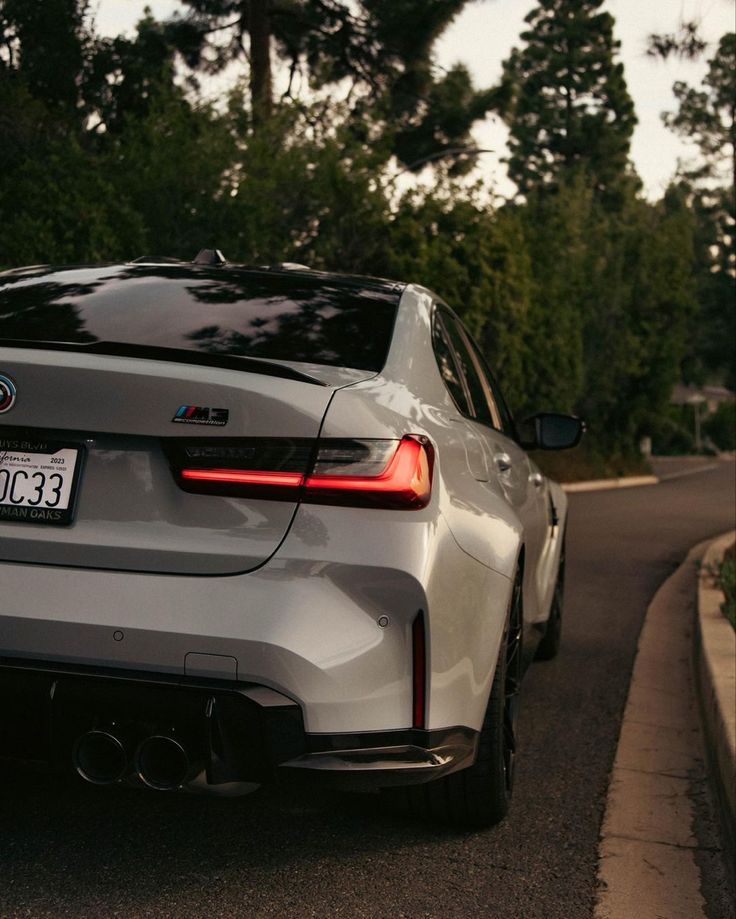 the back end of a silver car parked in front of a tree lined street with trees