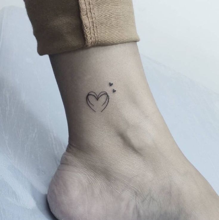 a small heart tattoo on the ankle is shown in black ink, and it has two hearts