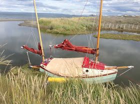 an old sailboat is sitting in the grass by the water's edge,