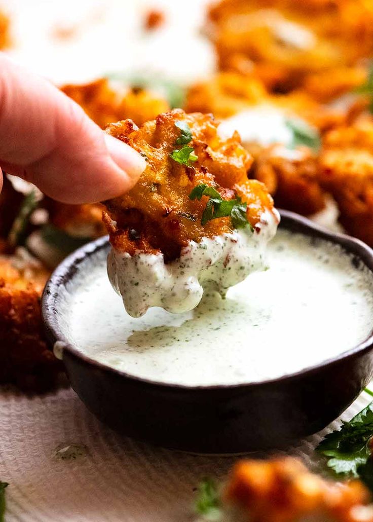 a hand dipping some food into a small black bowl filled with ranch dressing and garnished with cilantro