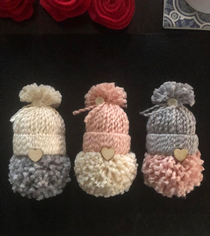 three knitted hats with hearts on them sitting next to some yarns and flowers