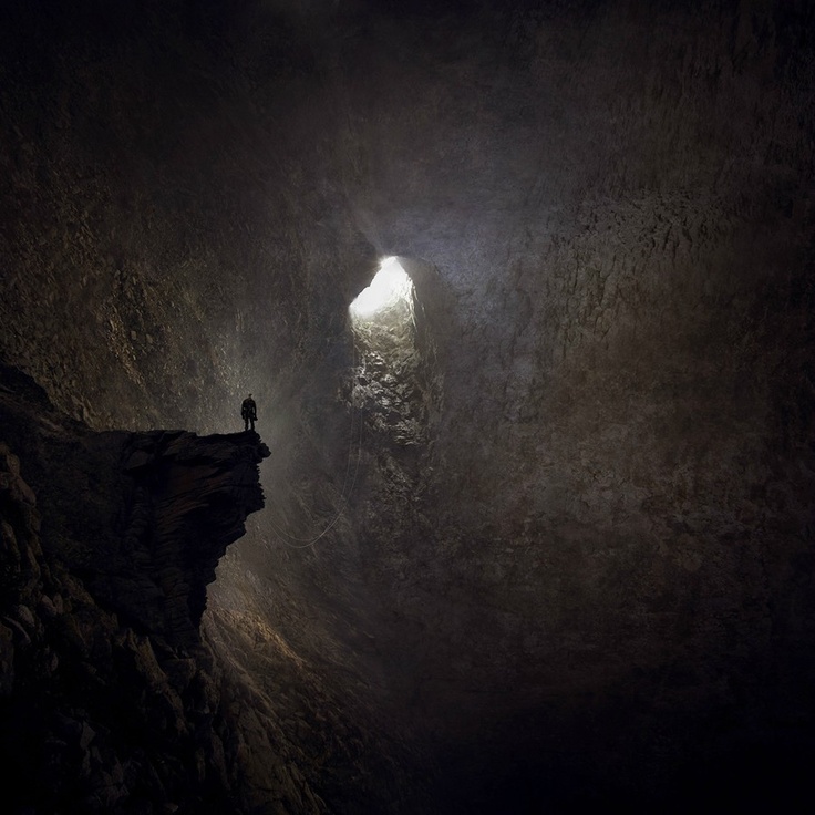 a person standing in the middle of a dark cave with light coming from behind it