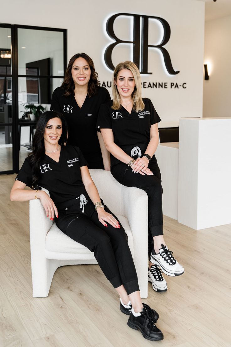 three women in black shirts are sitting on a white chair and posing for the camera