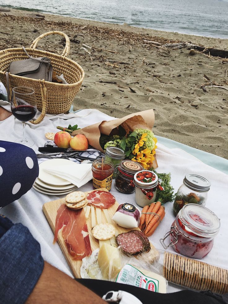 a picnic on the beach with ham, cheeses, and other foods laid out