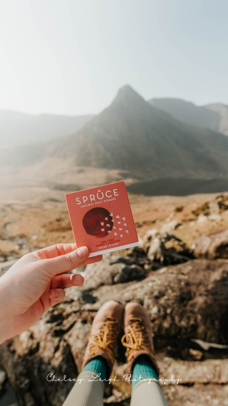 someone holding up a red card with the word sproce on it in front of some mountains