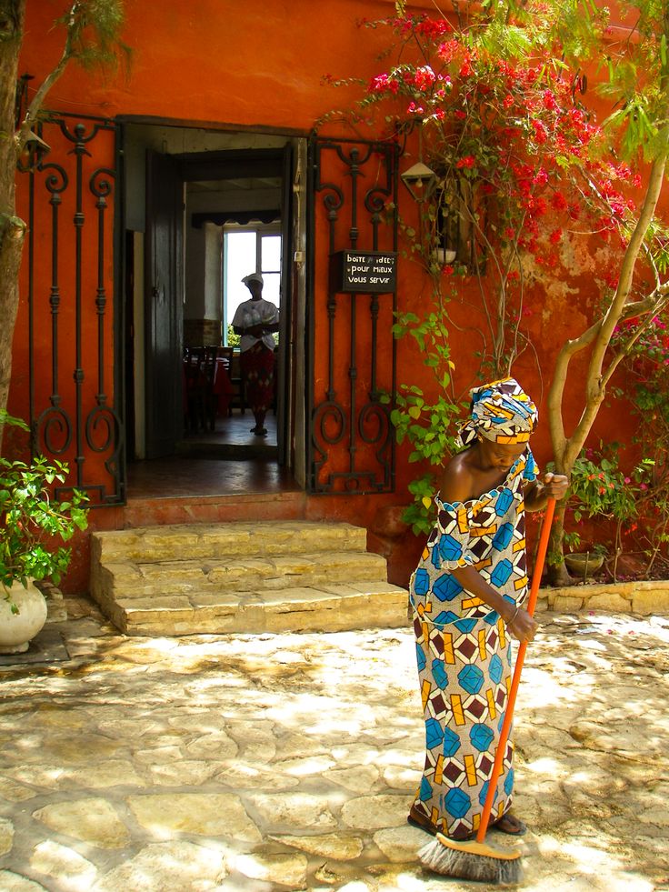 a woman standing in front of a red building holding a broom and potted plant