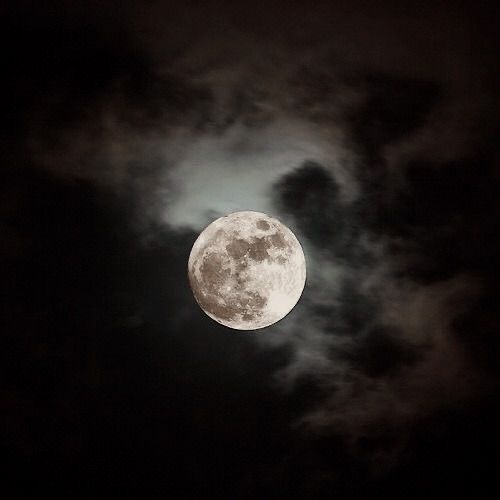 the full moon is seen through clouds in this dark night time sky with black and white colors