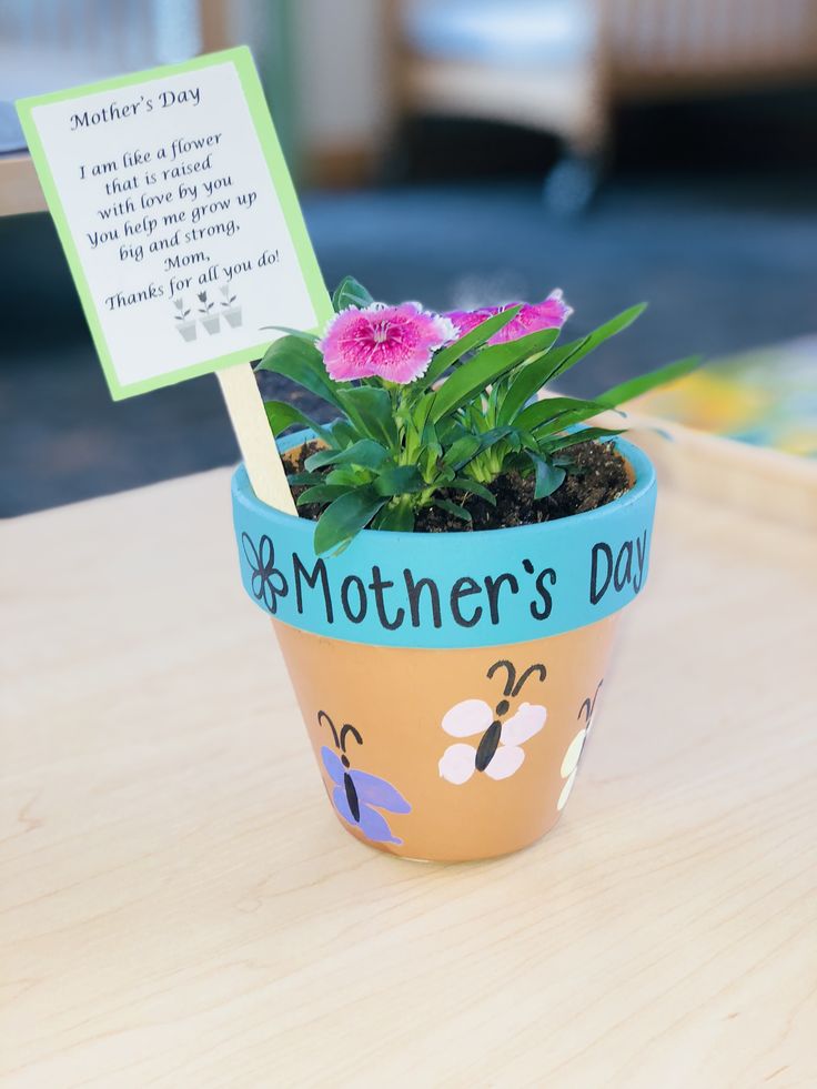 a small potted plant sitting on top of a wooden table next to a sign that says mother's day